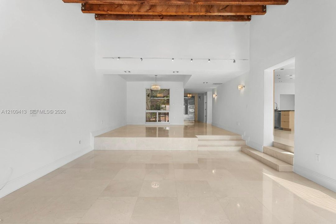Interior featuring exposed wood ceiling beams, polished stone tile flooring, multi-level tiered flooring, track lighting, and recessed ceiling lights
