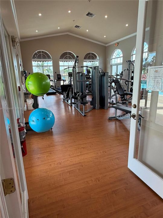 Fitness center featuring wood-finish flooring, vaulted ceilings with recessed lighting, and arched windows
