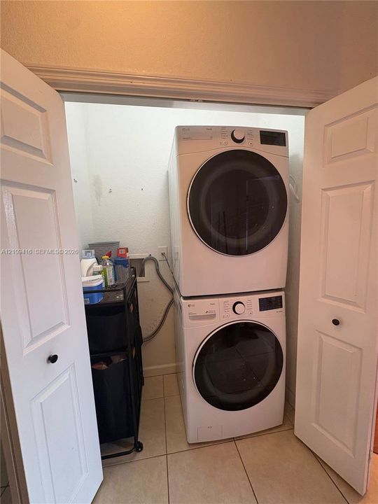 Laundry closet featuring stacked front-load washer and dryer units enclosed by paneled bifold doors and tile flooring