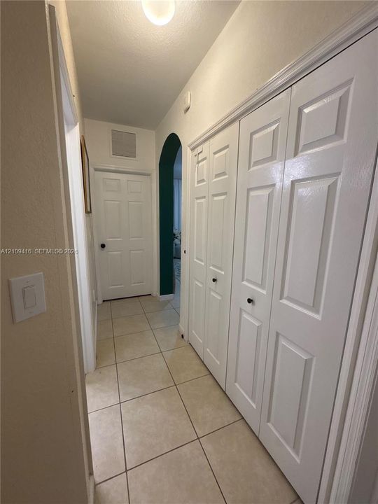 Hallway featuring neutral ceramic tile flooring, white six-panel closet doors, and an arched entryway