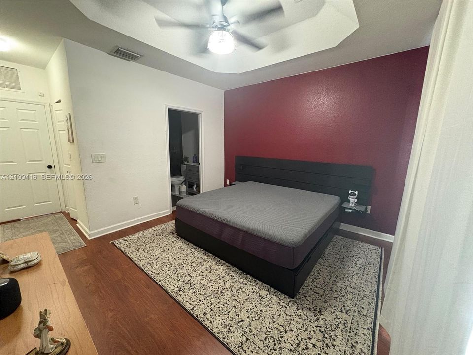 Tray ceiling with integrated ceiling fan, wood-finish flooring, and recessed accent wall