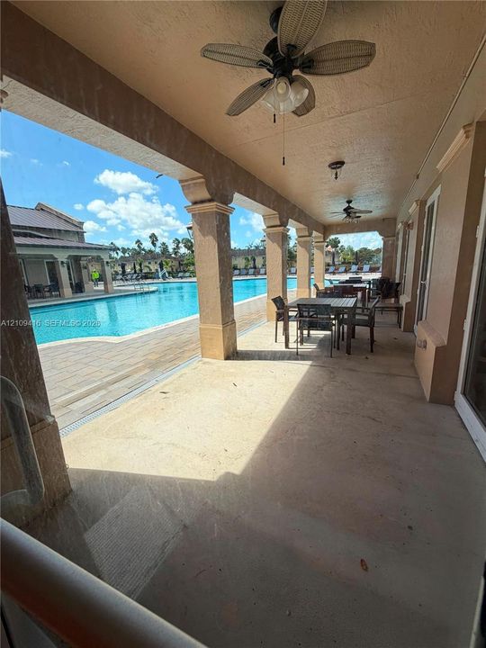Covered patio featuring concrete flooring, structured columns, and ceiling-mounted fans, overlooking a pool with stone paver decking