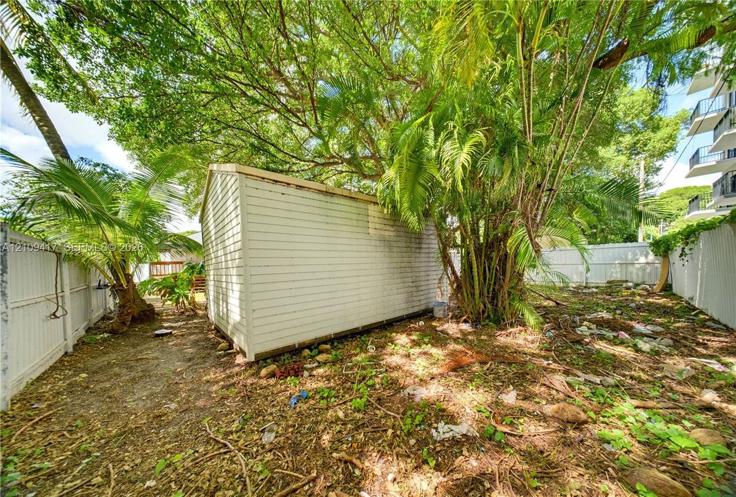 Exterior storage structure featuring horizontal siding, enclosed by perimeter vinyl fencing and mature vegetation
