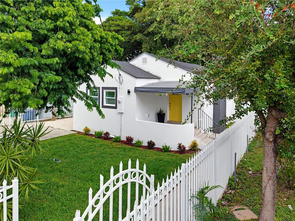 White stucco exterior featuring a covered front porch, low-maintenance landscaping, and decorative metal perimeter fencing