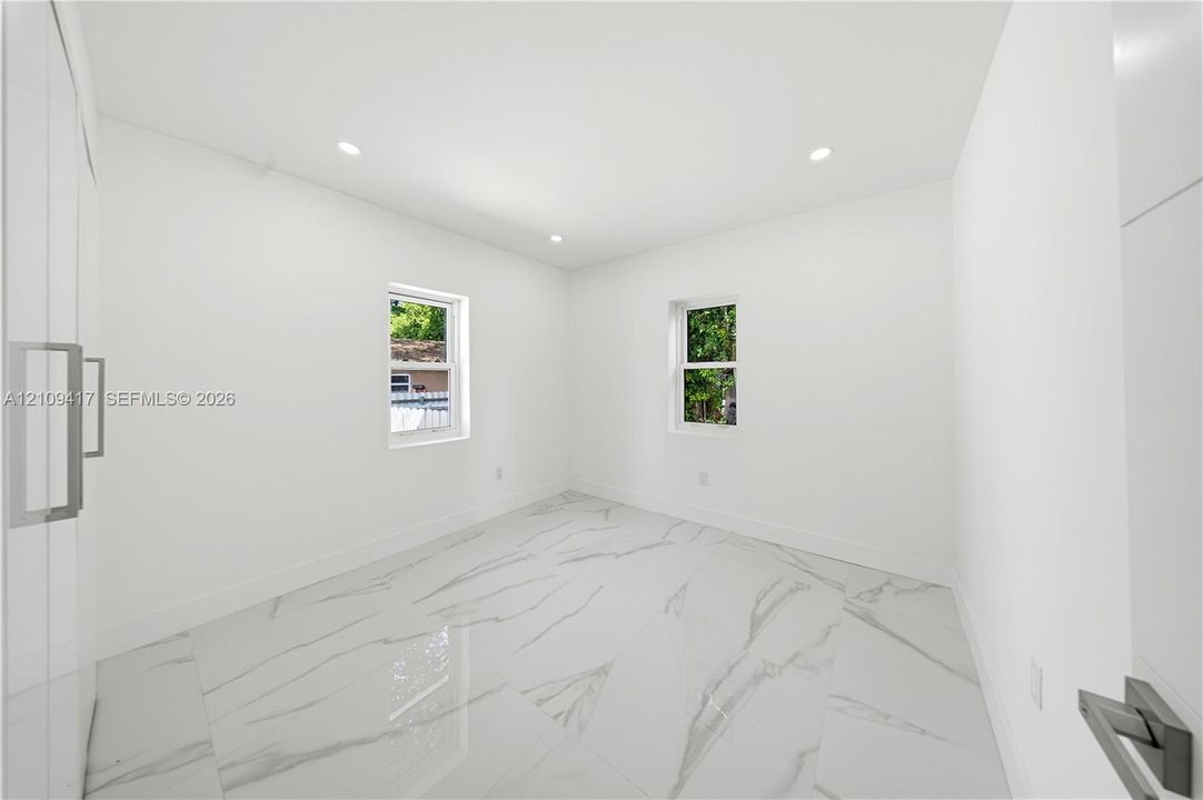 Bright room featuring high-gloss large-format tile flooring with veined detailing, recessed ceiling lighting, two double-hung windows, and full-height built-in cabinetry with metal pulls