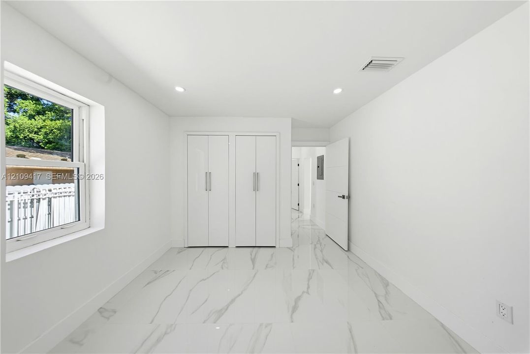 Interior room featuring large-format stone-finish tile flooring, dual built-in floor-to-ceiling closets with minimalist hardware, recessed lighting, and a single-hung window