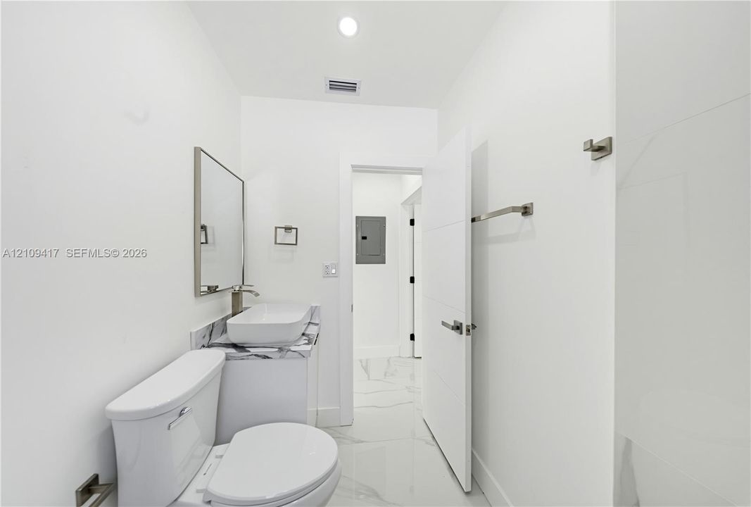 Bathroom featuring large-format tile flooring with a veined pattern, vanity with stone-finish countertop, rectangular vessel sink, wall-mounted faucet, and a frameless mirror