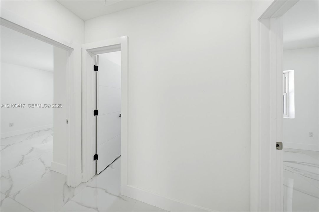 Interior featuring large-format white tile flooring with grey veining, solid-core interior doors, and matte black hardware