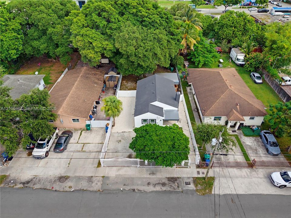 Aerial view of a residential property featuring a white exterior, dark roof, concrete driveway, and white perimeter fencing