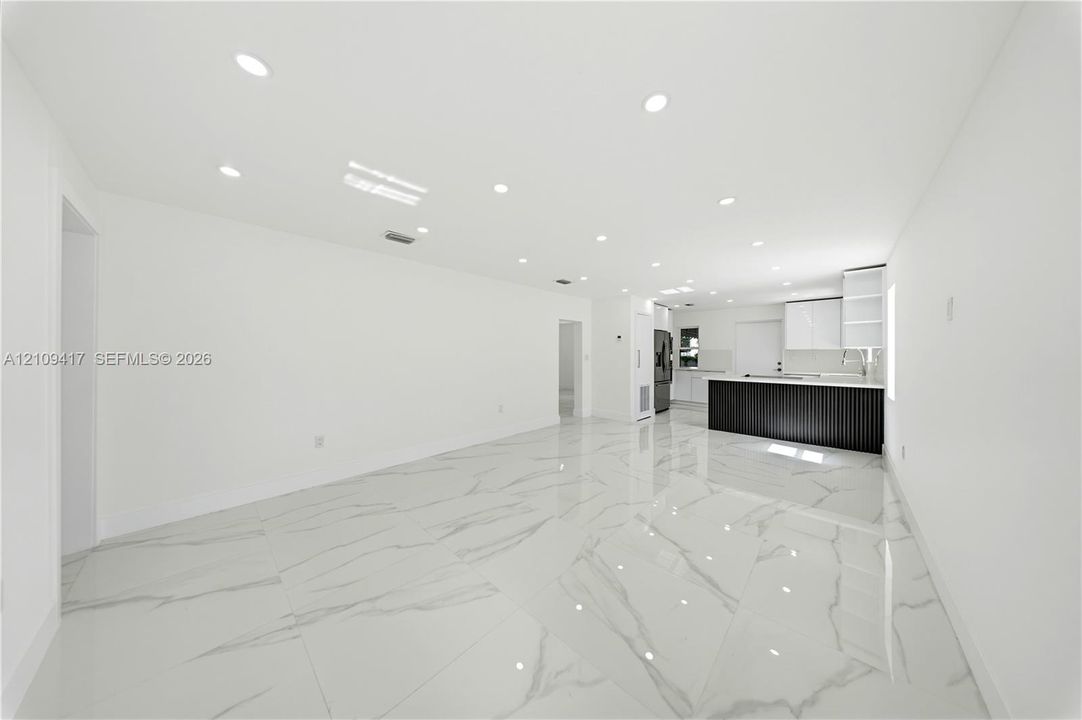 Open-concept interior featuring large-format stone-finish flooring, recessed lighting, and a kitchen equipped with a dark fluted-front island and white cabinetry