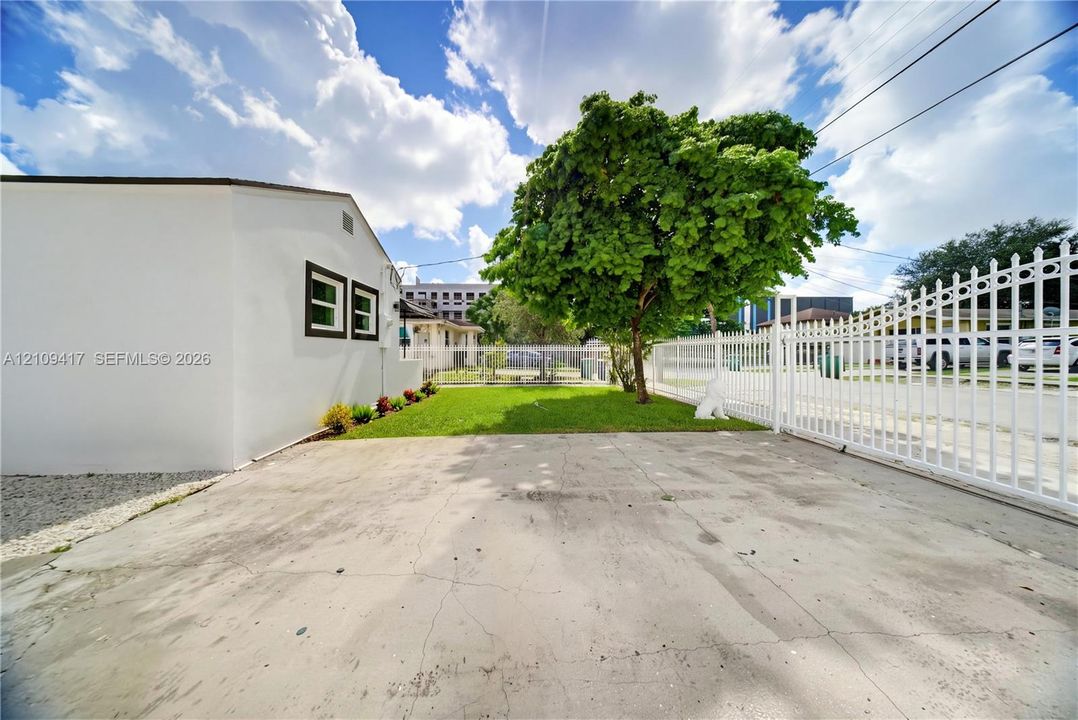 Concrete driveway featuring a metal perimeter fence, white exterior wall, and manicured lawn area
