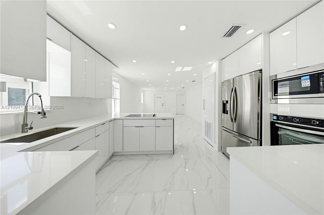 Contemporary kitchen featuring high-gloss white cabinetry, white stone-finish countertops, stainless steel appliances, and large-format porcelain tile flooring with grey veining