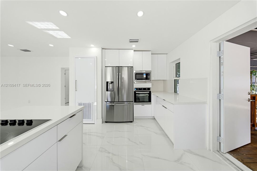 Kitchen featuring high-gloss white cabinetry, white stone-finish countertops, stainless steel appliances, recessed lighting, and large-format tile flooring with marble-style veining
