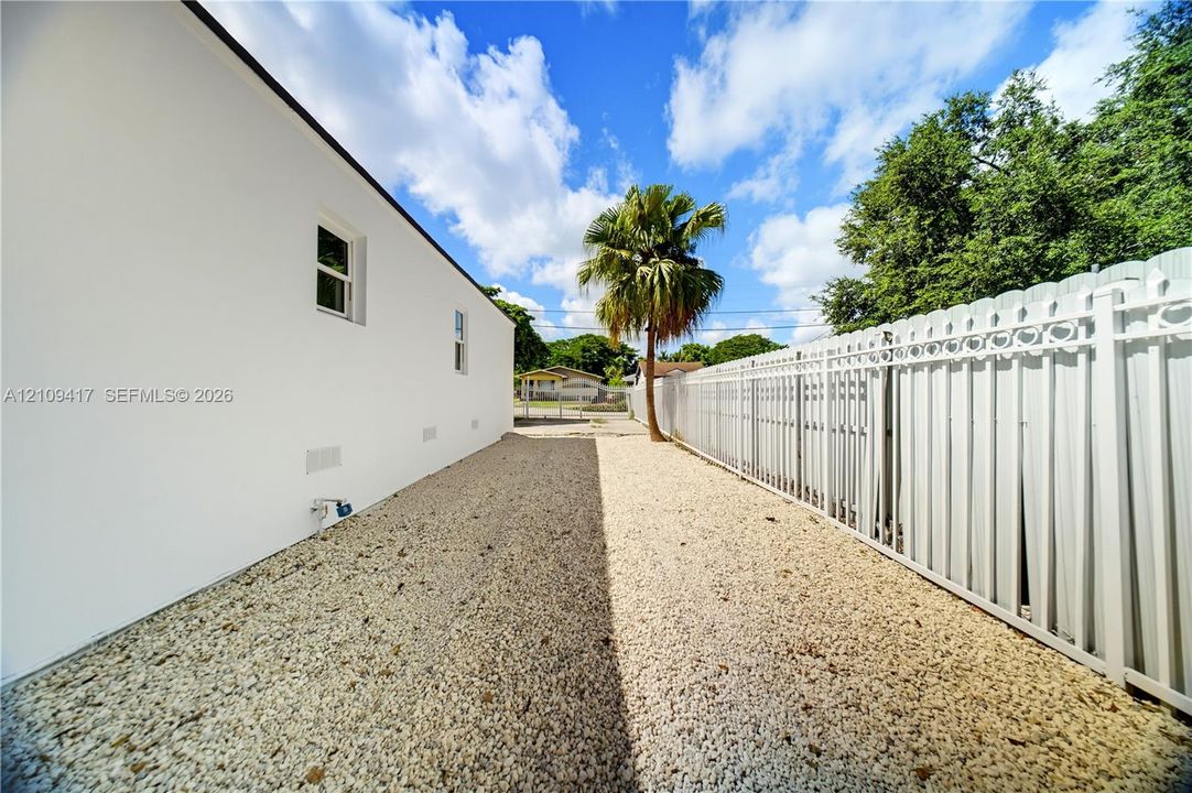 Side yard with white exterior wall, gravel ground cover, and full-height white vinyl privacy fencing