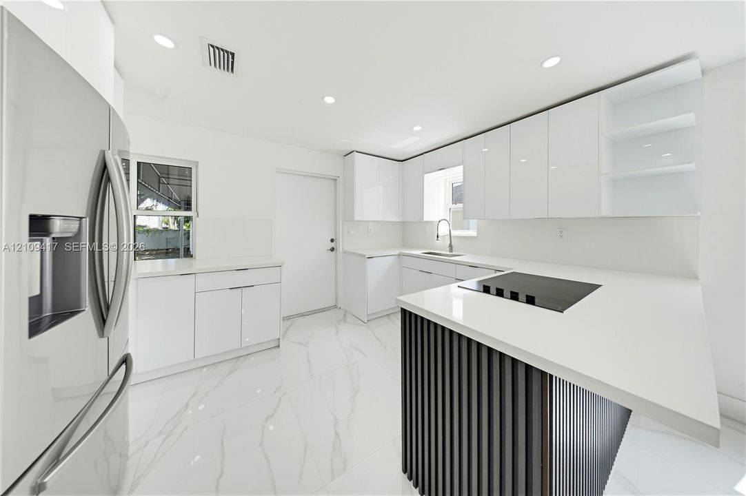 Kitchen featuring white gloss cabinetry, stone-finish countertops, an island with dark vertical paneling, stainless steel refrigerator, and stone-finish flooring