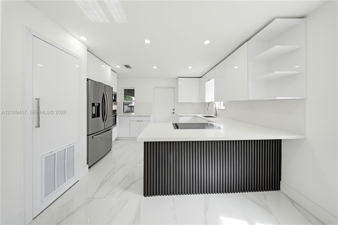 Contemporary kitchen featuring high-gloss white cabinetry, a kitchen island with a dark-finished vertical slat facade, stone-finish countertops, stainless steel appliances, and large-format tile flooring