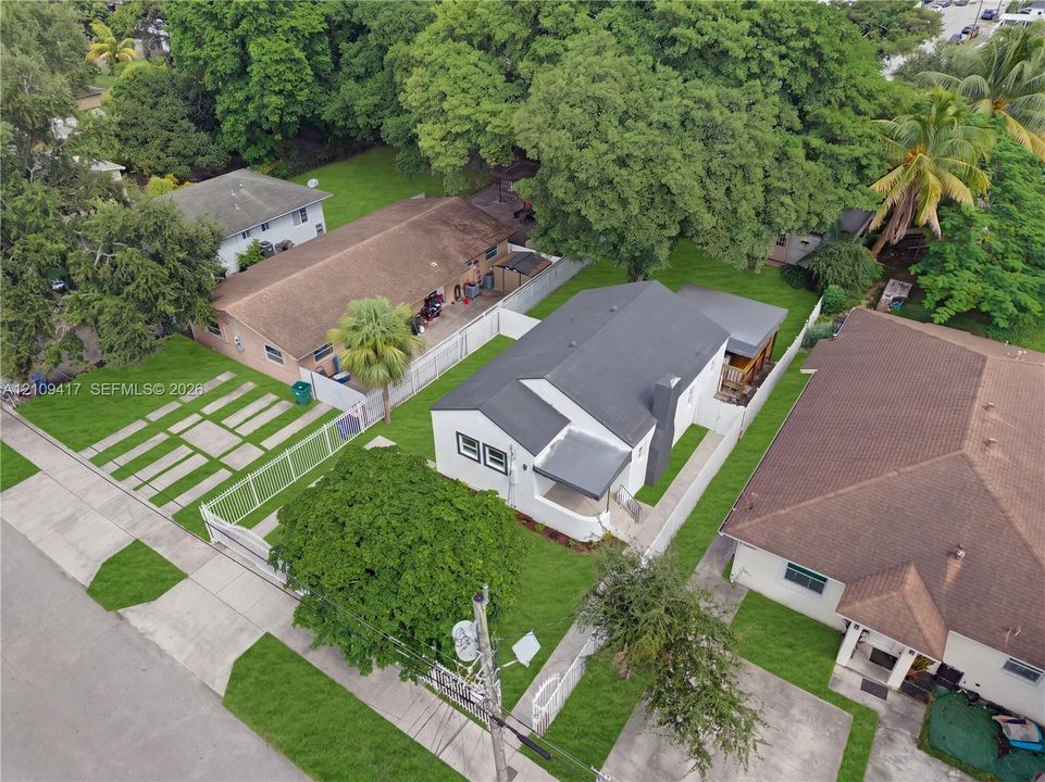 Single-story residence featuring a dark-toned pitched roof, exterior chimney, covered front porch, fenced perimeter, and mature canopy trees