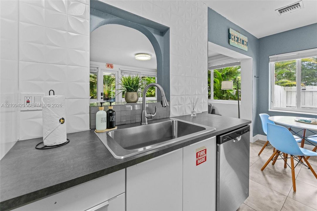 Kitchen featuring stainless steel undermount sink, gooseneck faucet, dark composite countertops, three-dimensional geometric tile backsplash, and stainless steel dishwasher