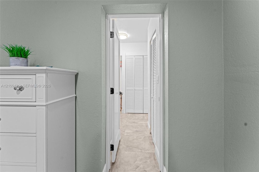 Neutral-toned interior walls featuring light-colored tile flooring and white louvered closet doors with flush-mount lighting