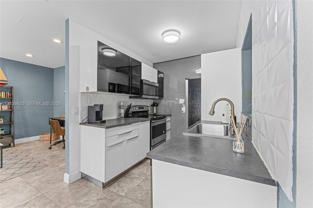 Kitchen featuring white slab-front cabinetry, dark solid-surface countertops, textured geometric tile backsplash, stainless steel appliances, and a high-arc pull-down faucet