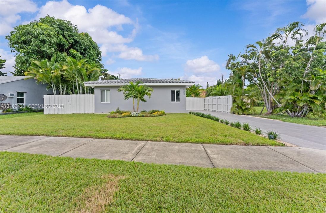 Single-story exterior featuring a gray stucco facade, a concrete tile roof, a manicured lawn, and perimeter privacy fencing