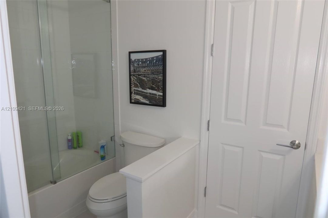 Bathroom featuring a glass shower panel, tub with tiled surround, and a white interior door with brushed metal hardware
