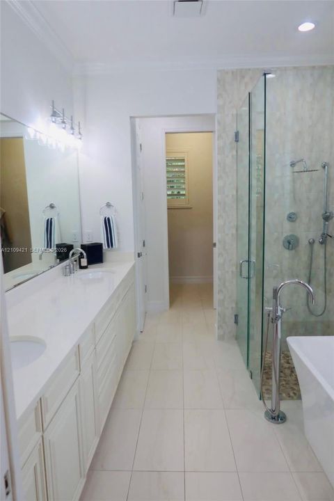 Dual-sink vanity with a solid-surface countertop, glass-enclosed walk-in shower with multi-head fixtures, freestanding soaking tub with floor-mounted faucet, and polished tile flooring