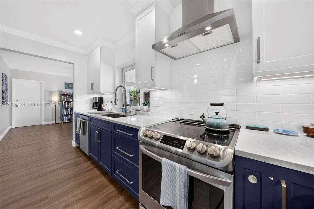 Kitchen featuring navy lower cabinetry, white upper cabinetry, stone-finish countertops, white subway tile backsplash, and stainless steel range hood