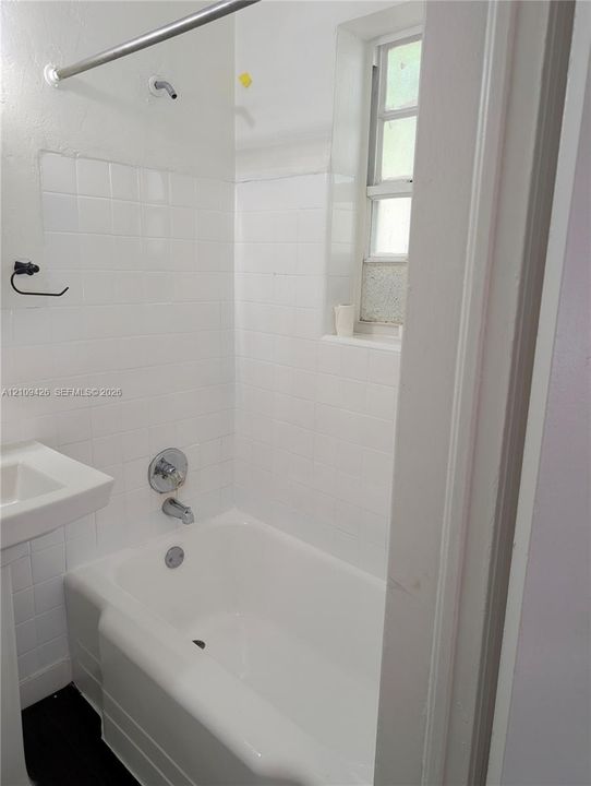 Bathroom featuring a white bathtub, white ceramic wall tile surround, pedestal sink, chrome hardware, and a vertical window