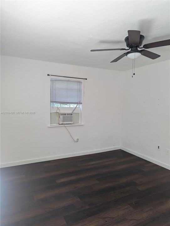 Room featuring wood-finish flooring, white walls, and a ceiling-mounted light fixture with a fan