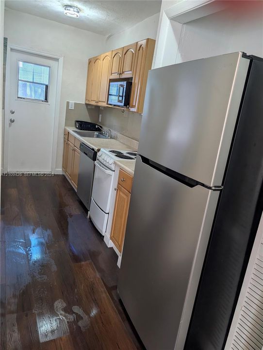 Kitchen featuring wood-finish flooring, shaker-style cabinetry, a stainless steel refrigerator, a built-in microwave, and an exterior door