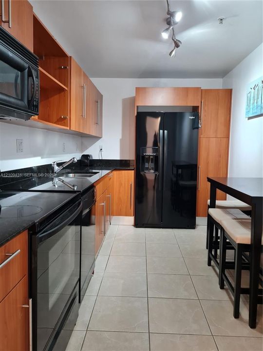 Kitchen featuring wood-finish cabinetry, dark solid-surface countertops, black appliances, tile flooring, and multi-directional track lighting