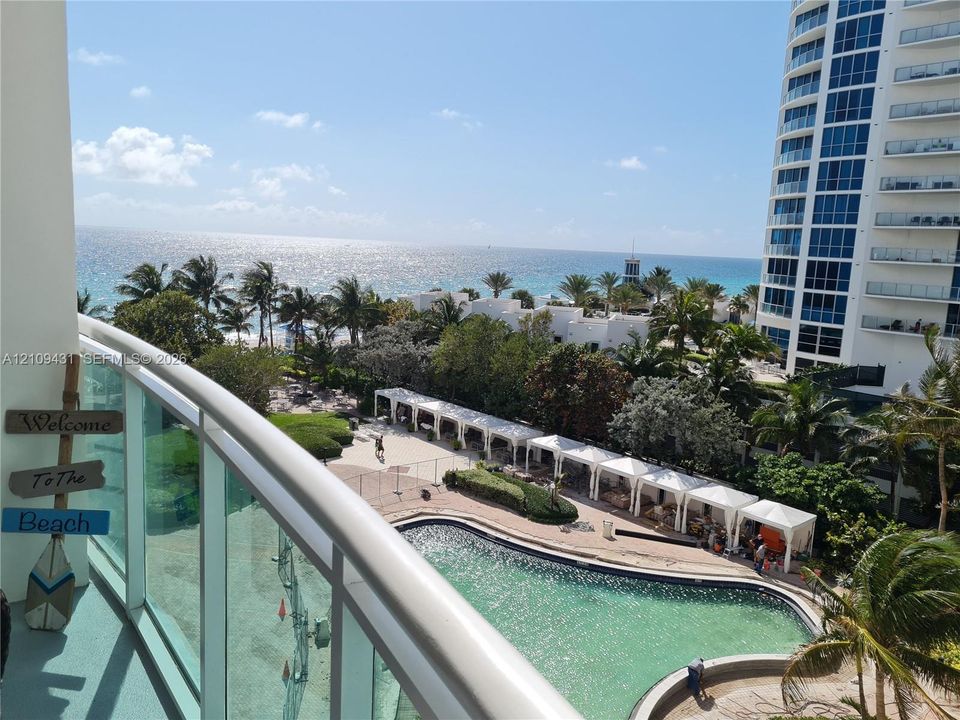 Balcony featuring a glass railing, overlooking an outdoor pool, cabanas, and ocean shoreline