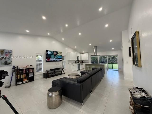 Vaulted ceilings featuring recessed lighting, large-format tile flooring, kitchen island with built-in cabinetry, and sliding glass doors
