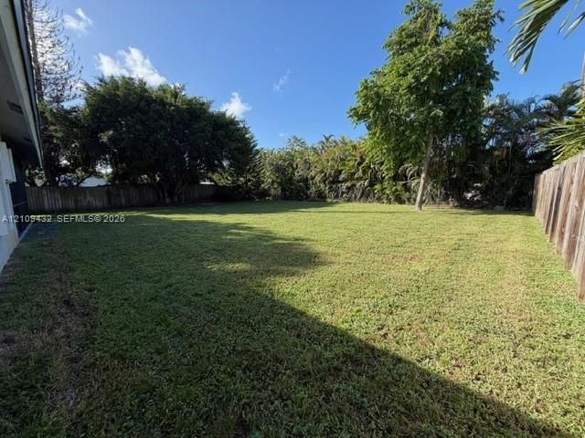 Expansive backyard featuring a large grass lawn, perimeter wood fencing, and mature trees