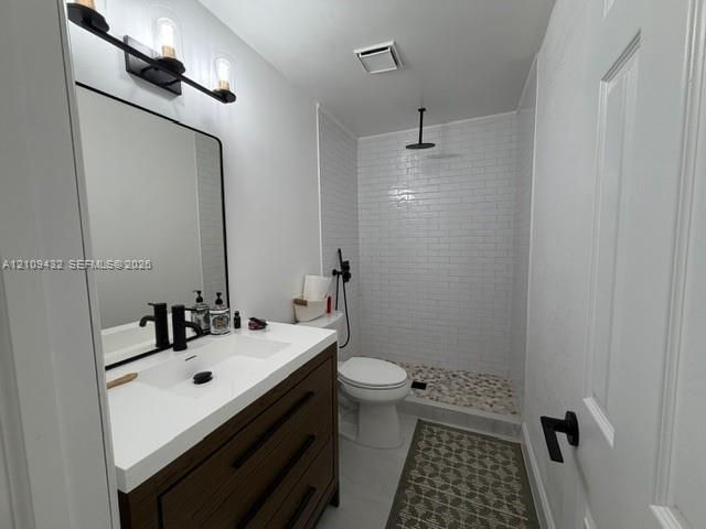 Bathroom featuring a dark wood-finish vanity with a white countertop, matte black fixtures, a walk-in shower with white subway tile, and stone-tiled shower flooring