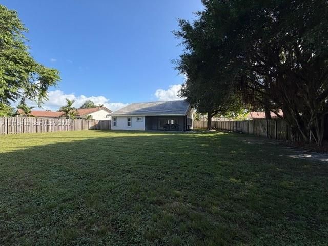 Expansive backyard featuring a large grass lawn, mature trees, and perimeter wood fencing