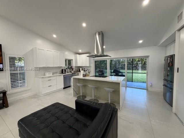 Kitchen featuring white shaker-style cabinetry, quartz countertops, a central island with a built-in cooktop, stainless steel range hood, and large-format tile flooring