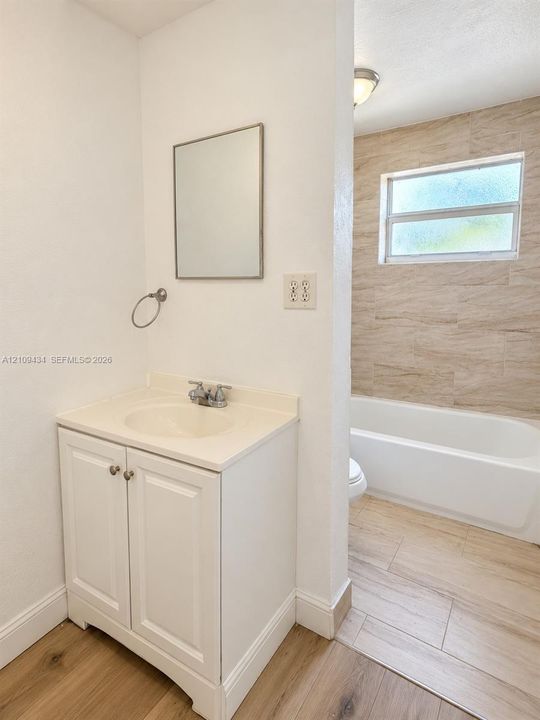 Bathroom vanity with a solid surface countertop, wood-finish flooring, and a tub enclosure featuring neutral stone-toned wall tile