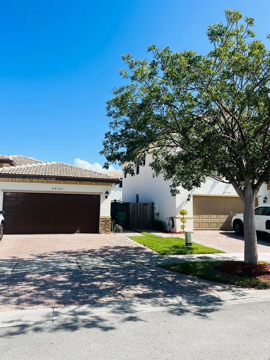 Multi-unit exterior featuring paved driveways, stone facade accents, tile roofing, and attached multi-car garages