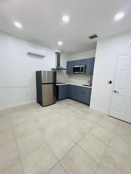 Kitchen featuring blue shaker-style cabinetry, stainless steel appliances, a chimney-style range hood, solid-surface countertops, and light-tone tile flooring