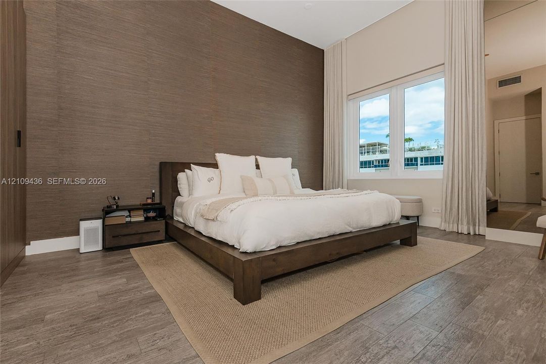 Textured accent wall, wood-finish flooring, vaulted ceiling, and full-length window treatments