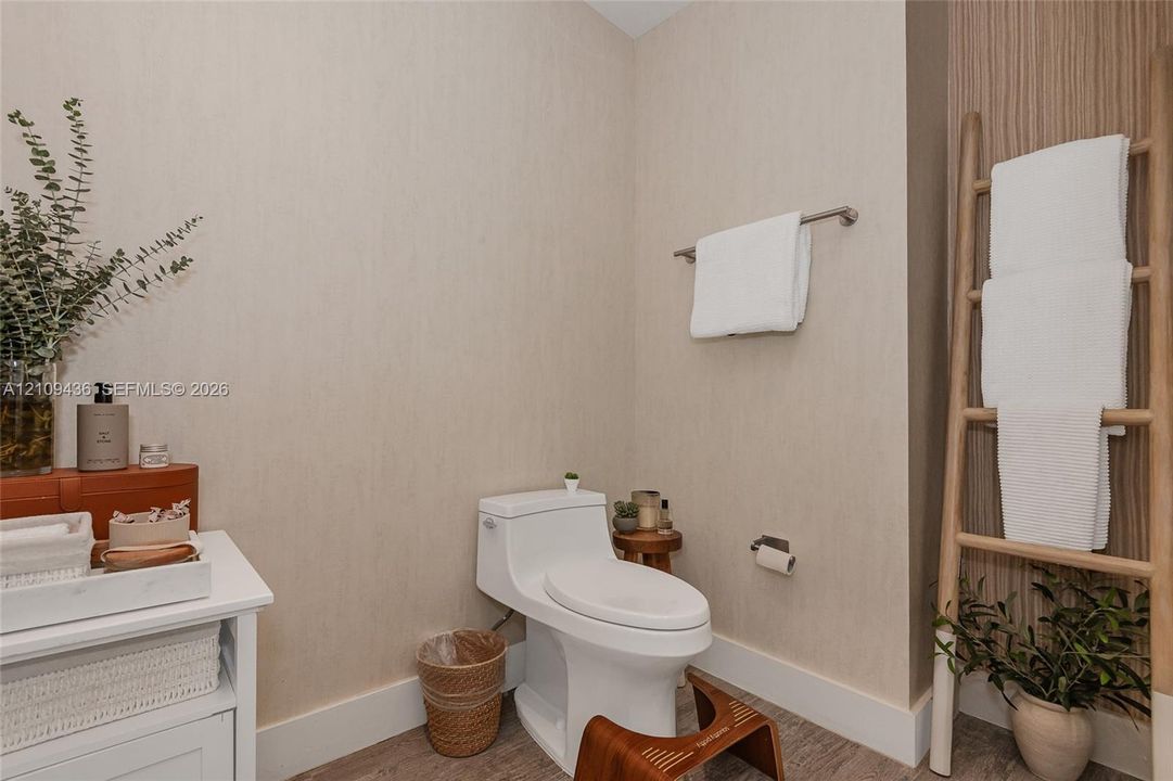Neutral-toned wallpaper, white one-piece toilet, wood-finish flooring, and vertical wood-slat accent paneling