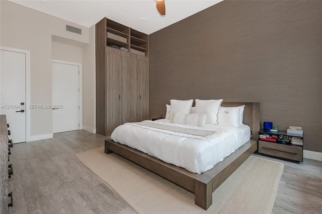 Floor-to-ceiling built-in wooden cabinetry, textured accent wall, wood-finish flooring, and a ceiling fan