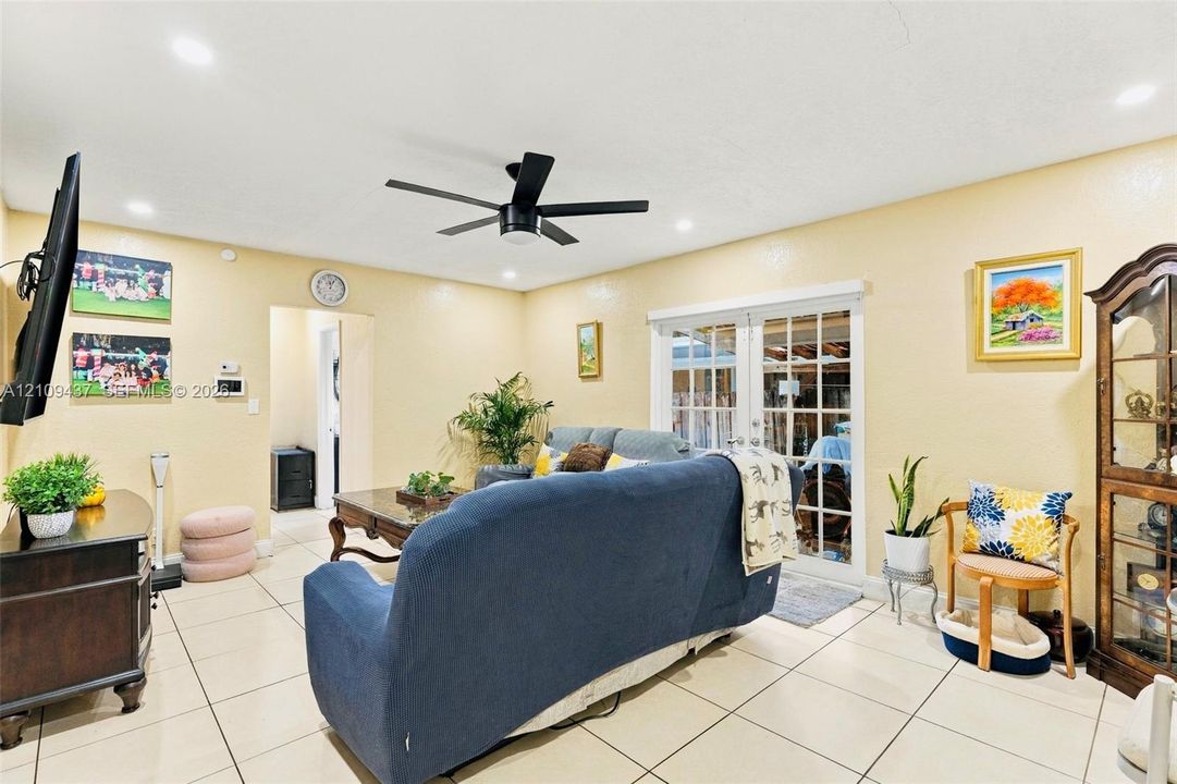 Interior space featuring large-format ceramic tile flooring, recessed ceiling lighting, a matte black multi-blade ceiling fan, and sliding glass doors with paneled inserts