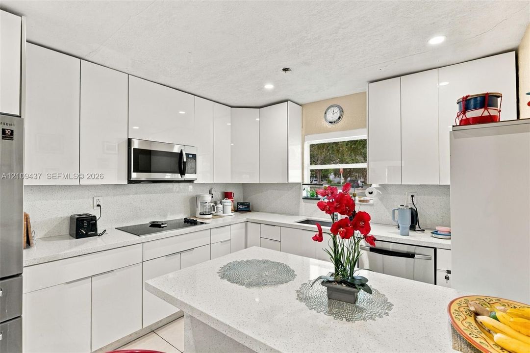 Kitchen featuring white gloss cabinetry, stone-finish countertops, stainless steel built-in appliances, recessed lighting, and an island