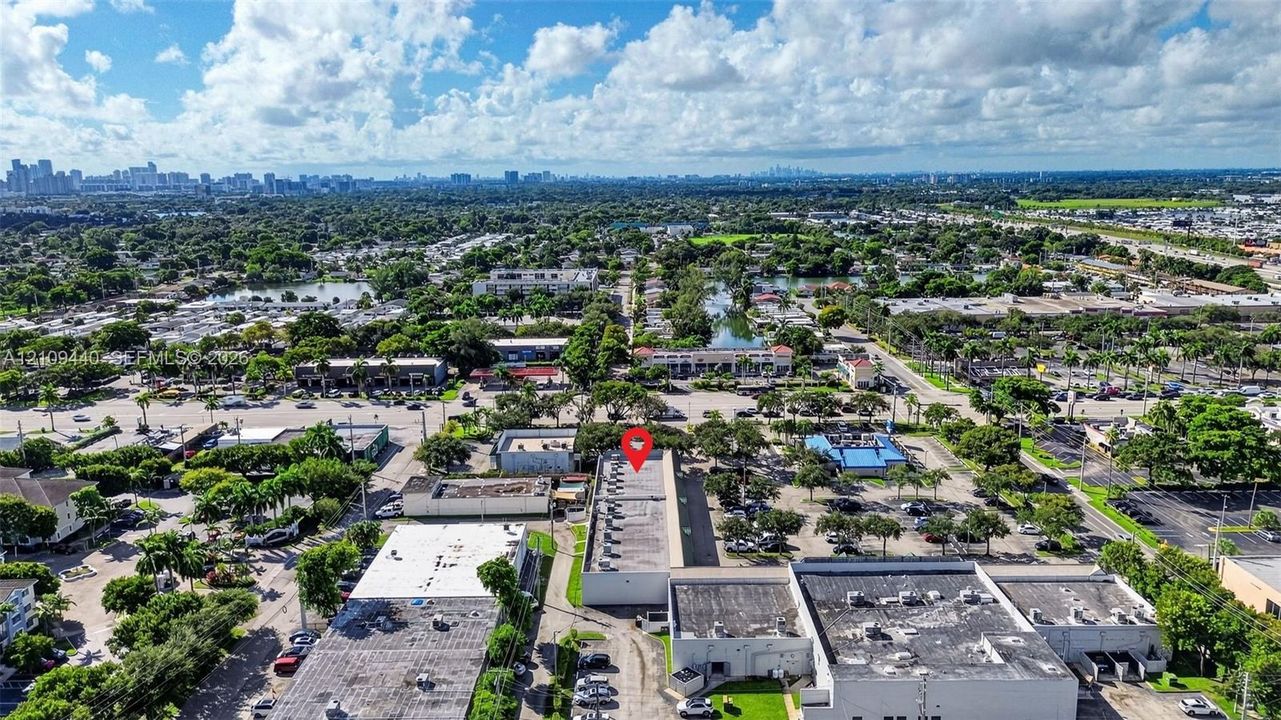 Aerial perspective of a commercial property featuring a flat-roof structure with rooftop HVAC units, multiple paved parking areas, and frontage on a primary thoroughfare