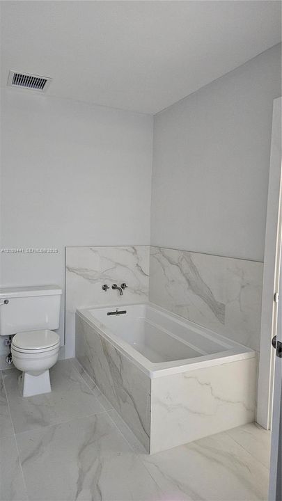 Bathroom featuring a deep soaking tub with a wall-mounted faucet, complemented by large-format tile flooring and matching tile surround