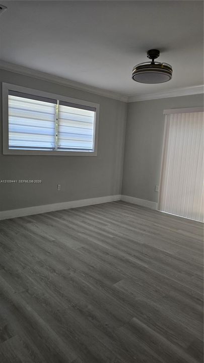 Interior space featuring wood-finish flooring, neutral wall paint, crown molding, a modern flush-mount ceiling fan, and sliding glass door access