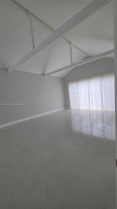 Vaulted ceiling featuring exposed structural beams, high-gloss tile flooring, and floor-to-ceiling windows